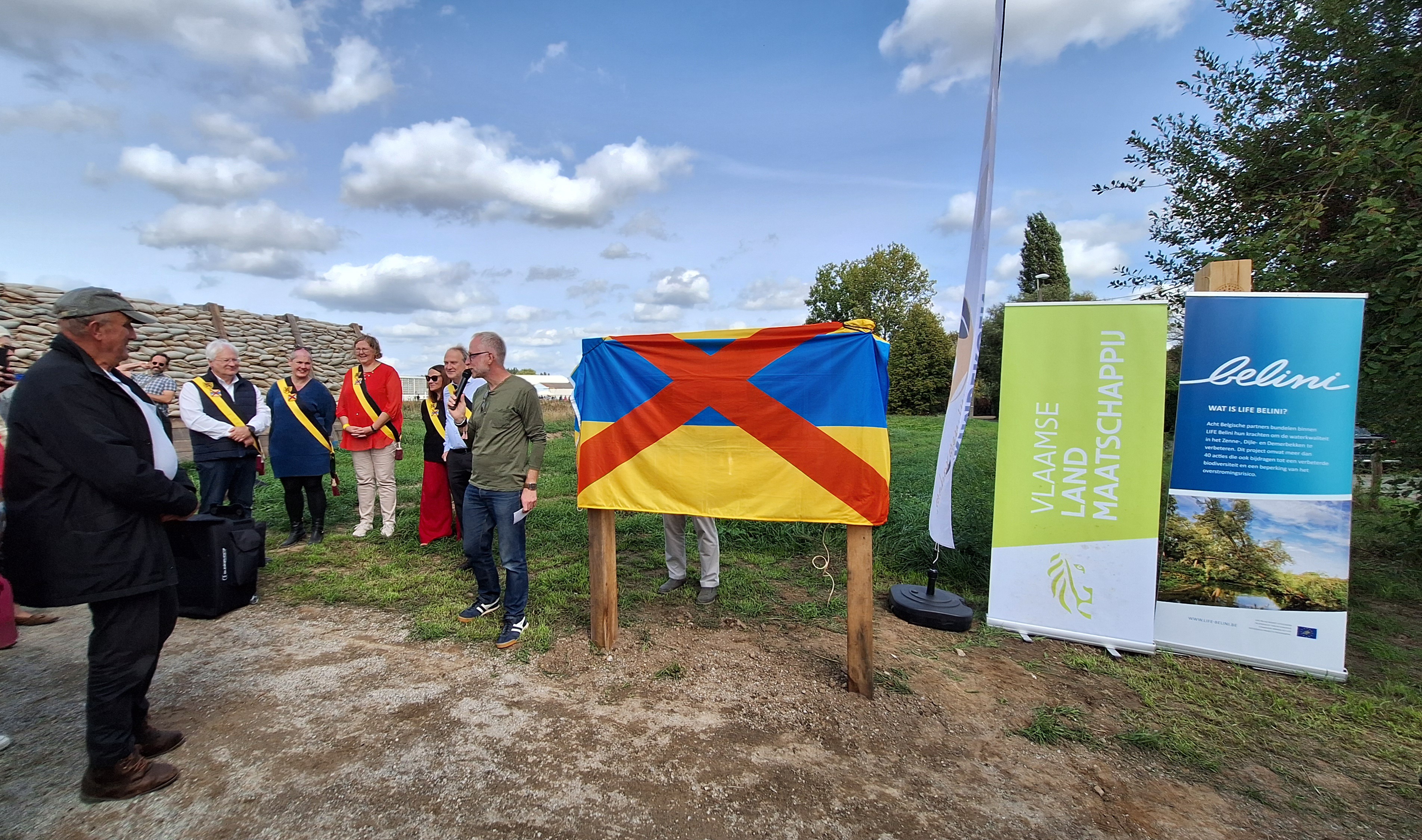 Foto toont speech projectamnager met daarnaast afgeplakt infobord  en banners VLM en Belini